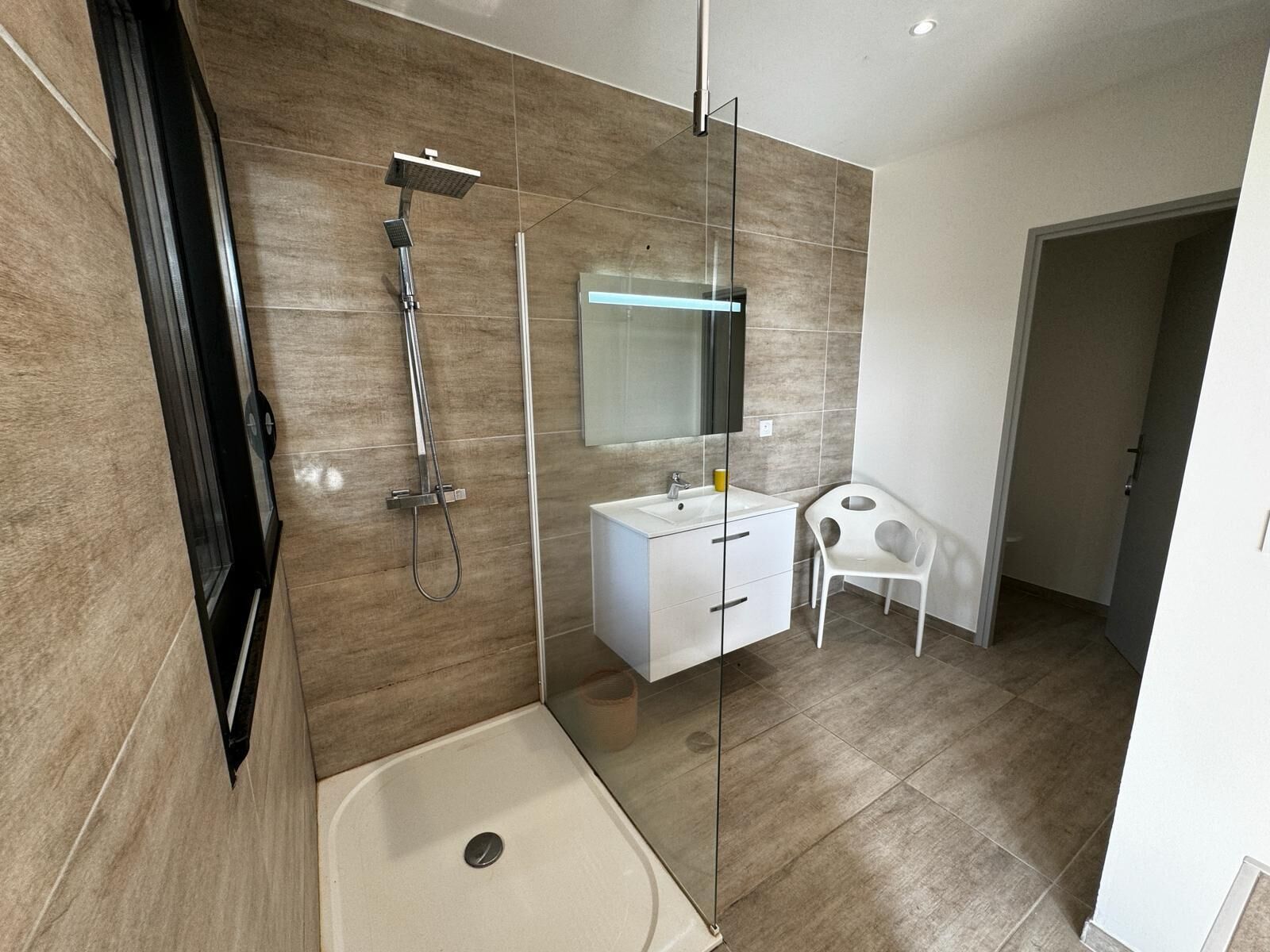 A modern bathroom with a glass shower enclosure, a white vanity, and a small white chair.