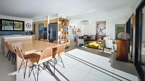 A modern kitchen with a large island, dining area with chairs, and a living room with a sofa and decorative items.
