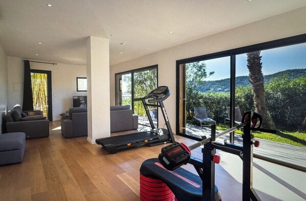 A spacious living area with a treadmill, a weight bench, and a large window offering a view of greenery. - MAGNIFICENT 330 M2 VILLA - HEATED POOL - SEA AND MOUNTAIN VIEWS (Conca)