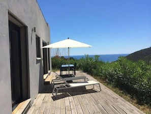 Relax on the deck with a view of the sea, surrounded by lush greenery.