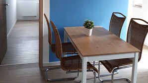 A dining area with a table and four wicker chairs, a potted plant, and a mounted television on a blue wall.