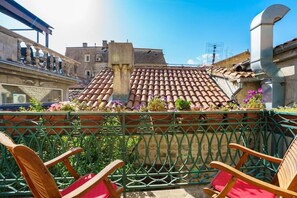 A rooftop terrace with terracotta tiles, a metal railing, and wooden chairs.