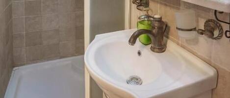 Un baño con ducha, lavabo, espejo y repisa con artículos de aseo.