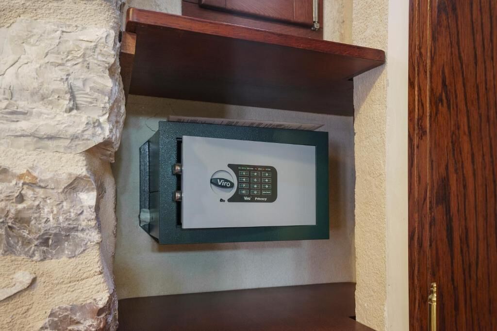 A Viro safe mounted on a textured wall with a wooden shelf above it.