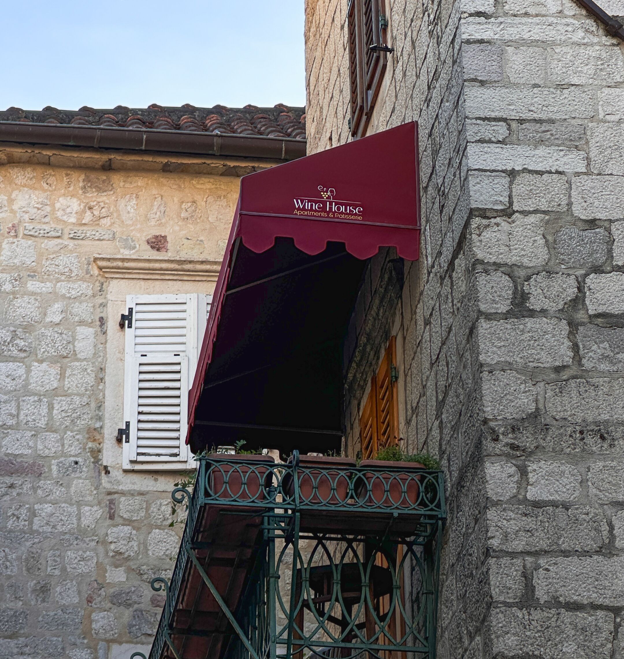 A building with a stone facade and a red awning labeled "Wine House Apartments & Patisserie."