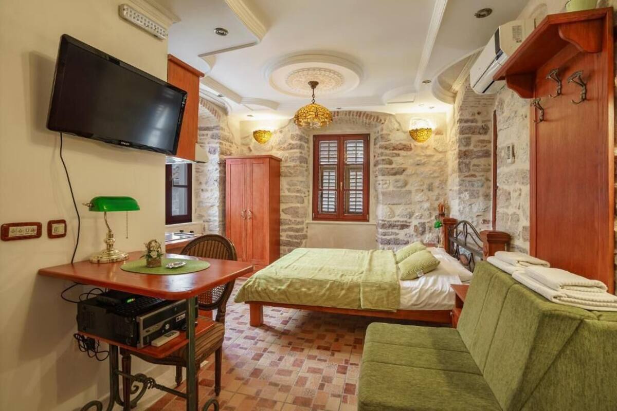 Une chambre à coucher avec un lit, un bureau avec un ordinateur, une télévision et des murs en pierre.