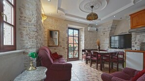 Un salon chaleureux avec un mur en pierre, un canapé, une table à manger avec des chaises, un téléviseur et une petite table avec une lampe.