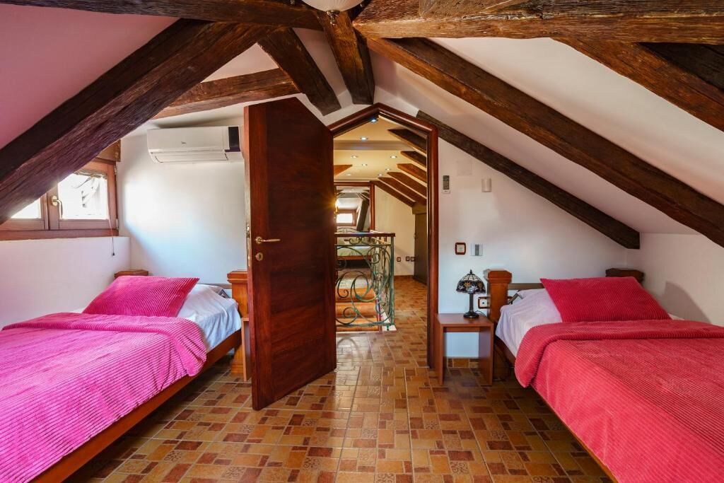 A bedroom with two beds, wooden beams, a tiled floor, and a door leading to another room.
