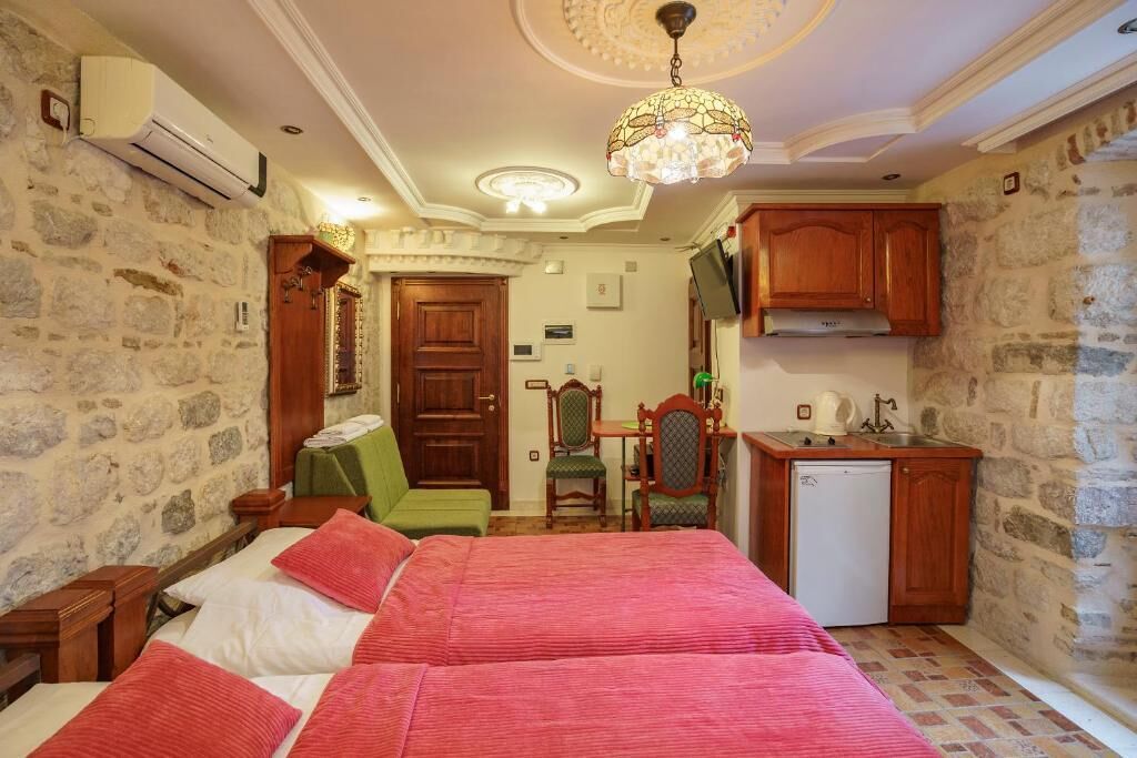 A compact room with a bed, a small kitchenette, and a stone wall.