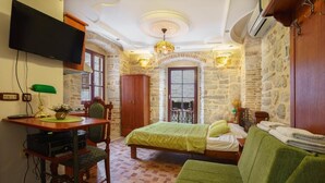 Une pièce confortable avec un lit, un canapé vert, un bureau avec une chaise, une télévision et des murs en pierre.