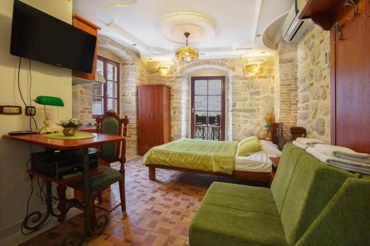 Une pièce confortable avec un lit, un canapé vert, un bureau avec une chaise, une télévision et des murs en pierre.
