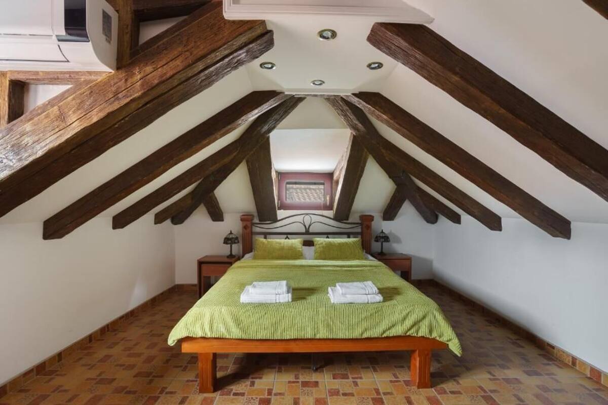 Une chambre avec un plafond en pente, un lit avec une literie verte et une tête de lit en bois.