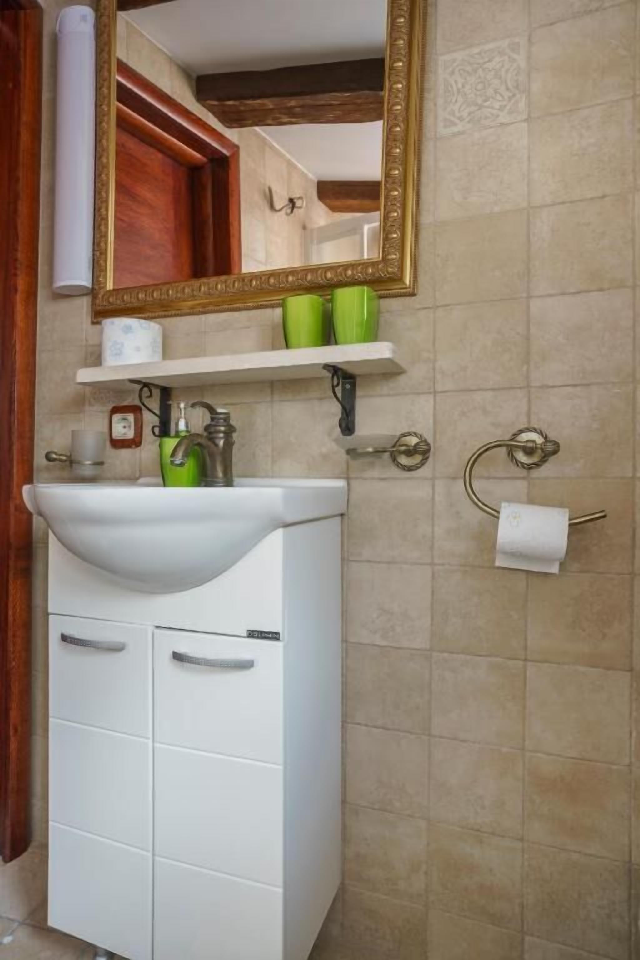 Een badkamer met een witte wastafel, een groene zeepdispenser en een spiegel met gouden lijst.