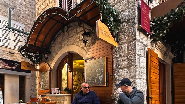 Un café en plein air avec des murs en pierre, des volets en bois et une enseigne indiquant qu’il s’agit d’une pâtisserie.