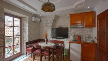 Cocina compacta con comedor, paredes de piedra, armarios de madera, un televisor integrado y un refrigerador pequeño.