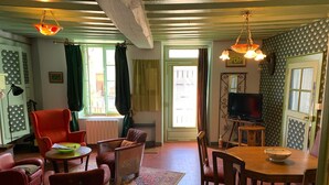A cozy living room with a fireplace, a television, and a dining area with a table and chairs. - Alfred and George, The Appendix (Sainpuits)