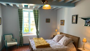 A cozy bedroom with a bed, a chair, a window with curtains, and a lamp. - Alfred and George, The Appendix (Sainpuits)