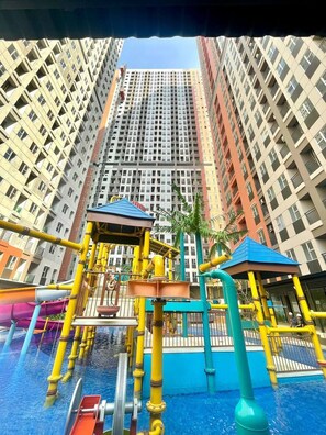 A playground with slides and climbing structures, surrounded by tall residential buildings. - transpark juanda by red promo (Bekasi)