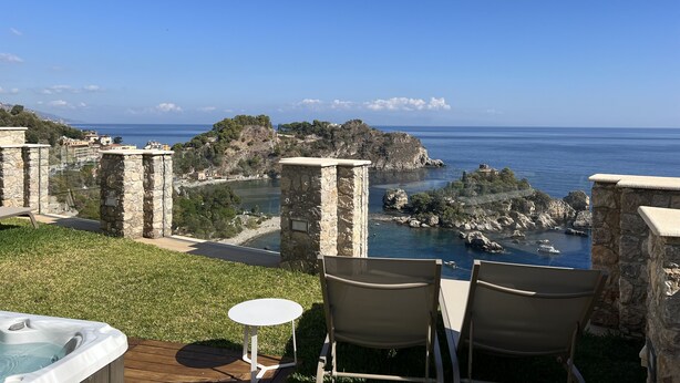 Une terrasse dotée d’un jacuzzi, de chaises et offrant une vue sur la mer et la côte rocheuse.