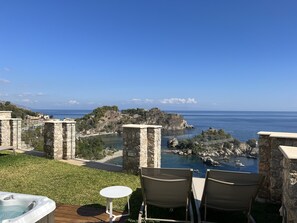 Eine Terrasse mit Whirlpool, Stühlen und Blick auf das Meer und die felsige Küste.