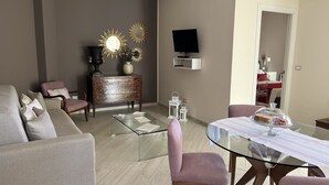 Un salon moderne avec une table basse en verre, un canapé, un téléviseur fixé au mur et un coin repas comprenant une table et des chaises en verre.