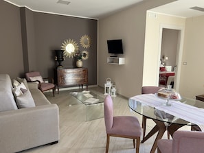 Ein modernes Wohnzimmer mit einem Glastisch, einer Couch, einem an der Wand befestigten Fernseher und einem Essbereich mit einem Glastisch und Stühlen.