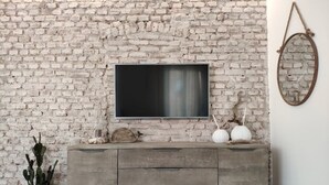 A rustic living room with a brick wall, a flat-screen TV mounted above a wooden cabinet, and a hanging mirror. - Vanilla House Design, Garage, Wifi (Sestri Levante)