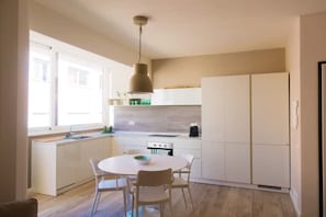 Een moderne keuken met witte kasten, een ronde eettafel en een hanglamp.