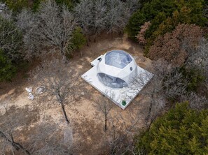 A dome-shaped structure with a glass ceiling, surrounded by trees and a sandy ground.