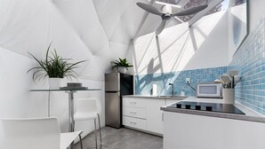 Une cuisine moderne avec une table en verre, des chaises blanches, un réfrigérateur, un four à micro-ondes et un pare-feu en carreaux bleus.
