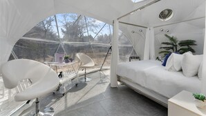 Une chambre moderne aménagée comme une tente, avec un lit, deux chaises, une petite table et une plante en pot.