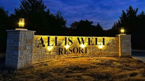 Une enseigne en pierre portant l'inscription « ALLIS WELL RESORT » est illuminée au crépuscule.