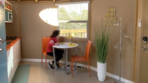 A compact kitchen with a window, a table, and chairs. There's a potted plant and a sign on the wall. - Hippy Chick Yurt Cabin (Saint Jo)