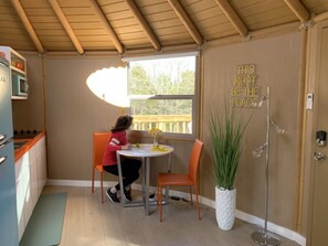 A compact kitchen with a window, a table, and chairs. There's a potted plant and a sign on the wall.