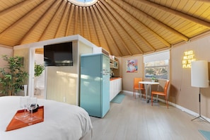 Una habitación compacta con cama, kitchenette, comedor y un amplio ventanal.