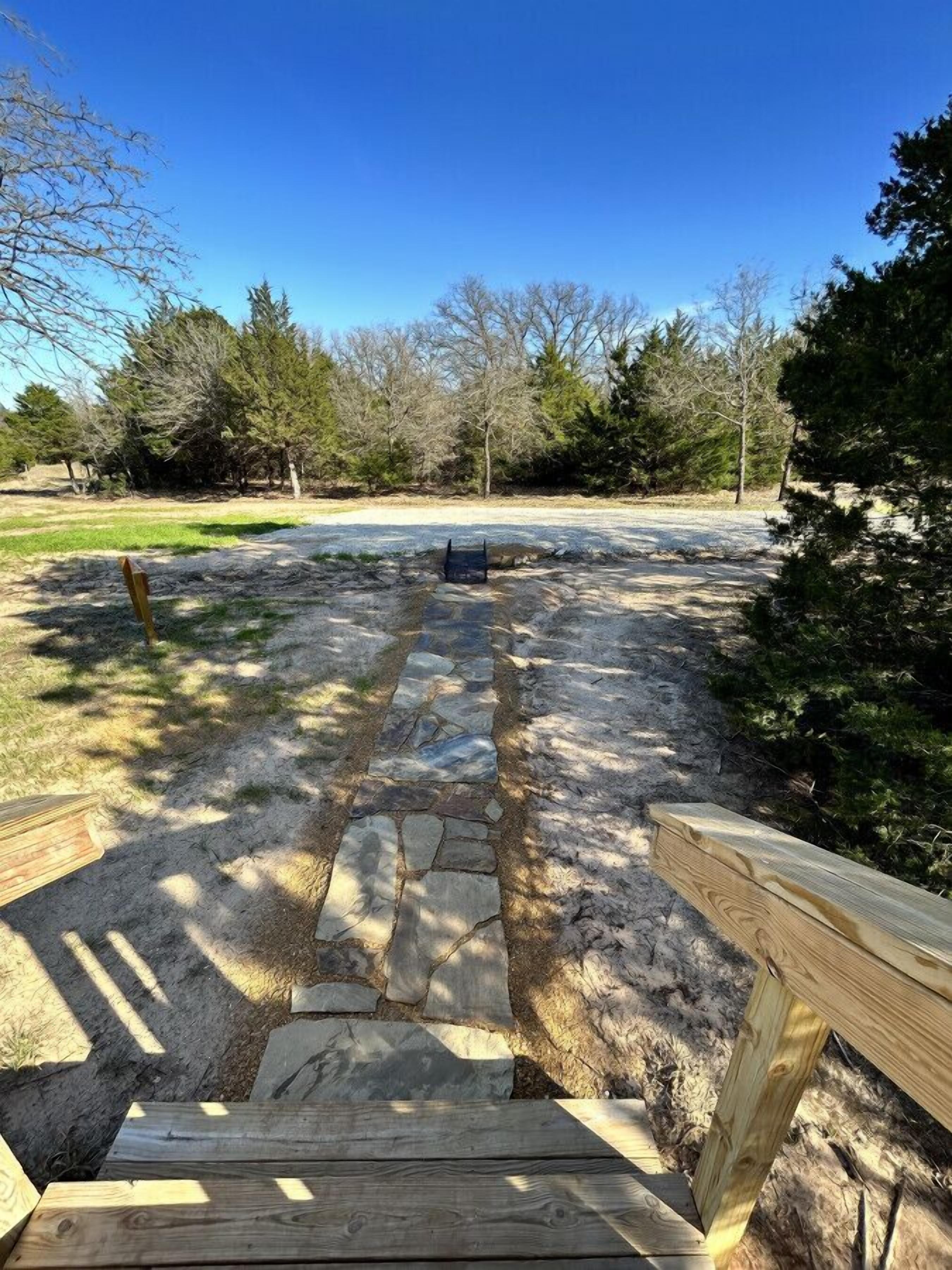 Una terraza de madera con escalones de piedra que conducen a una zona cubierta de césped rodeada de árboles.