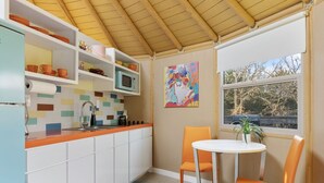 A kitchen with white cabinets, a colorful backsplash, a microwave, and a dining area with a table and chairs. - Hippy Chick Yurt Cabin (Saint Jo)