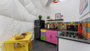 Cuina compacta amb una estructura blanca semblant a una tenda, un refrigerador negre, un microones i un relleu de rajoles de colors.