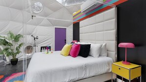 Una habitació moderna en forma de tenda amb un llit, una taula petita, una làmpada i una planta en test.