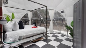 A tented room with a bed, a glass table, a lamp, and a potted plant. - The Starman Dome (Saint Jo)