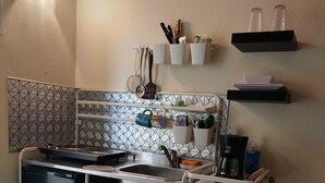 Cozinha compacta com lava-louças, fogão e pia. Utensílios pendurados na parede, cafeteira e prateleira com garrafas.