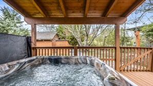 A hot tub under a wooden deck with a view of a house and trees. - Cabin in the Valley! Easy Access! Pet Friendly! (Sevierville)