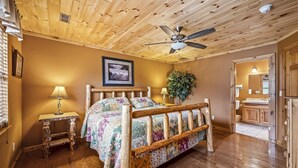 A wooden-framed bed with a floral bedspread in a room with wooden floors and a ceiling fan. - Cabin in the Valley! Easy Access! Pet Friendly! (Sevierville)