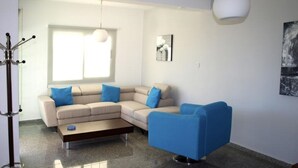 A modern living room with a beige sectional sofa, a blue armchair, and a coffee table. - Luxury, Modern Villas with private pool & garden in Coral Bay area (Πέγεια, Πάφος)
