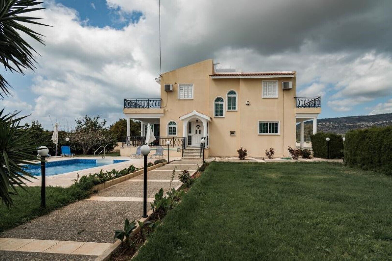 A two-story house with a swimming pool, a well-maintained lawn, and a view of the surrounding landscape.