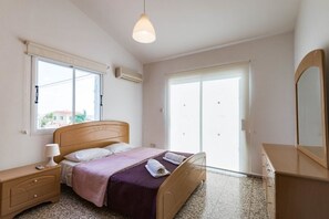 A bedroom with a bed, bedside table, lamp, and a dresser.