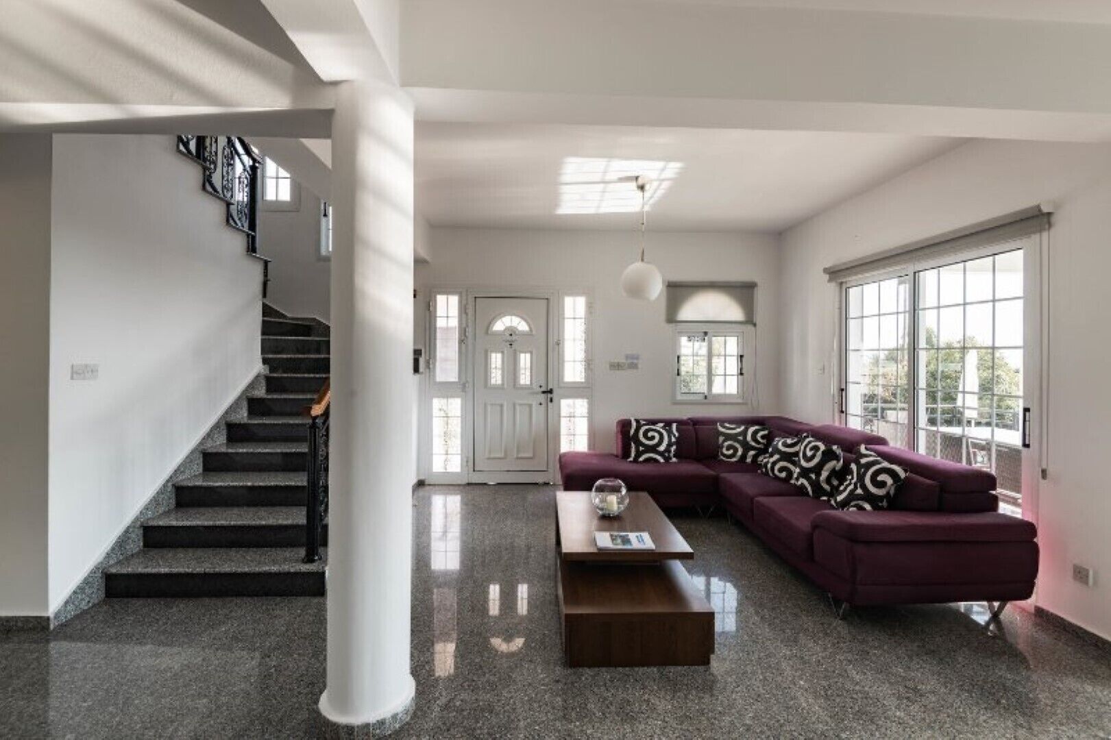A spacious living area with a staircase, a large window, and a modern sofa.
