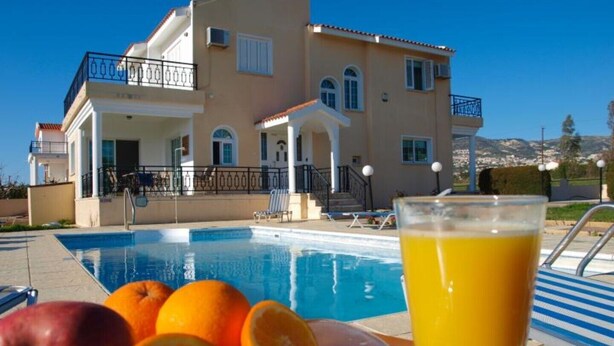 A poolside view of a two-story building with a swimming pool, fruit, and a glass of orange juice. - Luxury, Modern Villas with private pool & garden in Coral Bay area (Πέγεια, Πάφος)