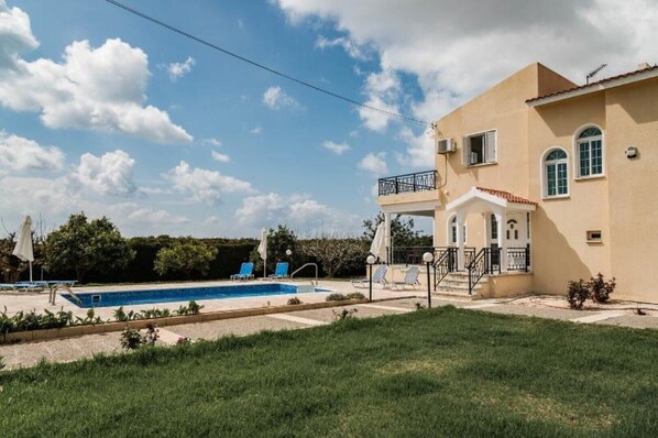 A two-story building with a swimming pool, a covered patio, and a well-maintained lawn.