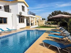 A swimming pool with lounge chairs, a covered seating area, and a building with balconies. - Luxury, Modern Villa with private pool & garden in Coral Bay area (Πέγεια, Πάφος)